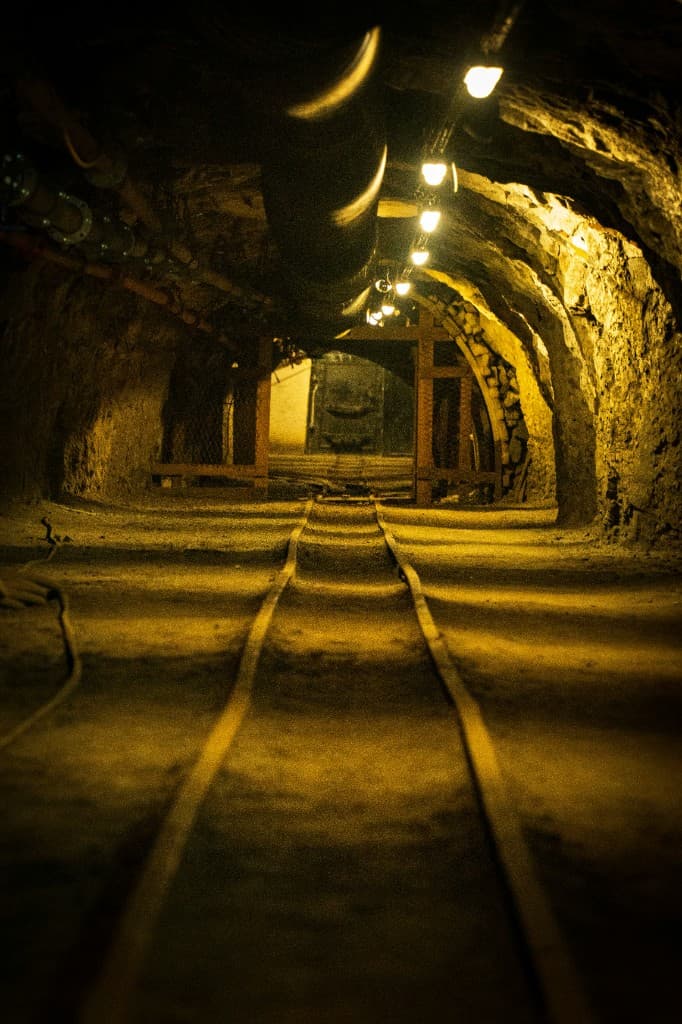 A lit underground tunnel with rails in the floor.