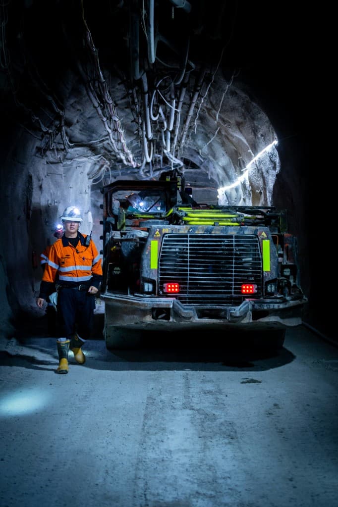 An operator walking beside an underground loader in a mine tunnel.