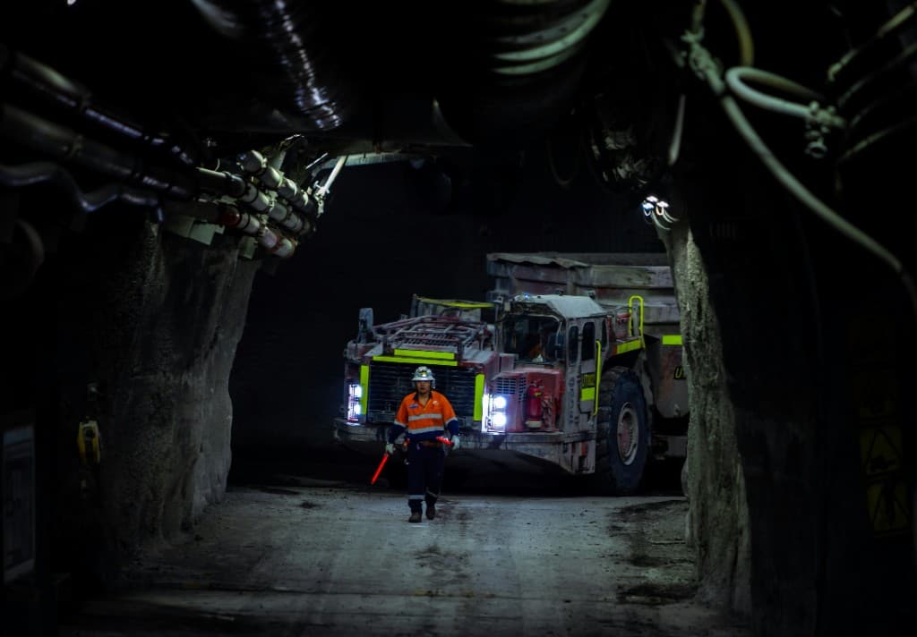 A worker with a light stick in front of a haul truck underground.